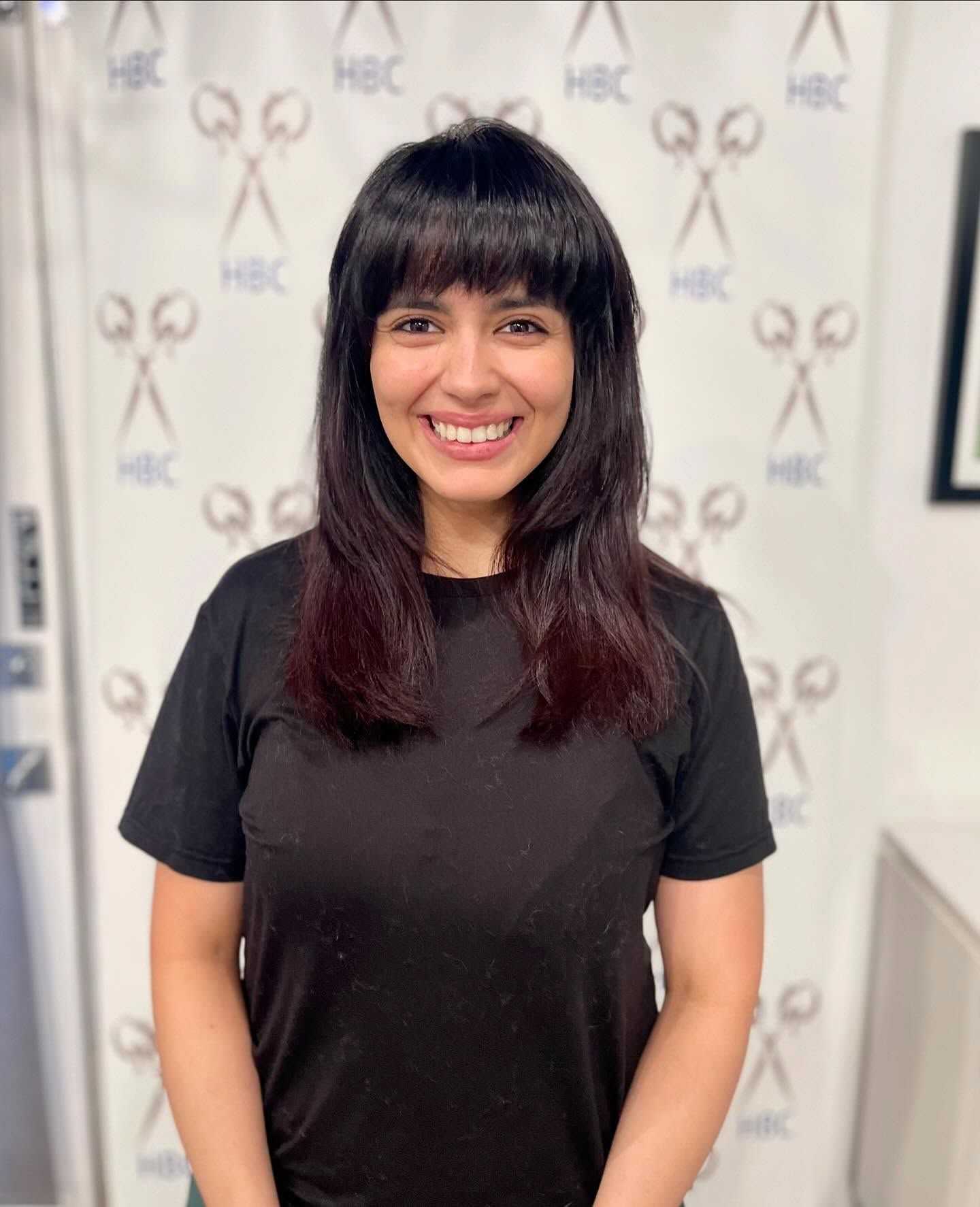 Smiling woman with long hair in front of scissors-themed backdrop.